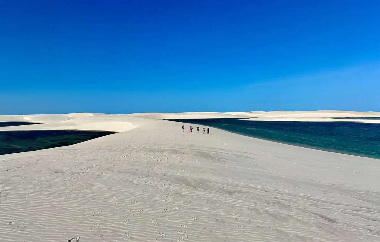 Turistas caminhando entre lagoas emendadas nas dunas do Parque Nacional dos Lençóis Maranhenses